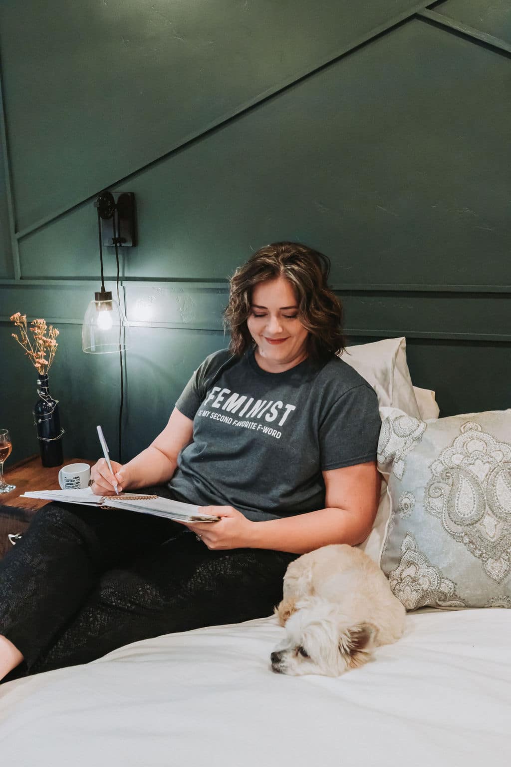 Angella sitting on her bed against a dark green wall with her two favorite things: her Soul Vision Planner and her dog, Sadie.