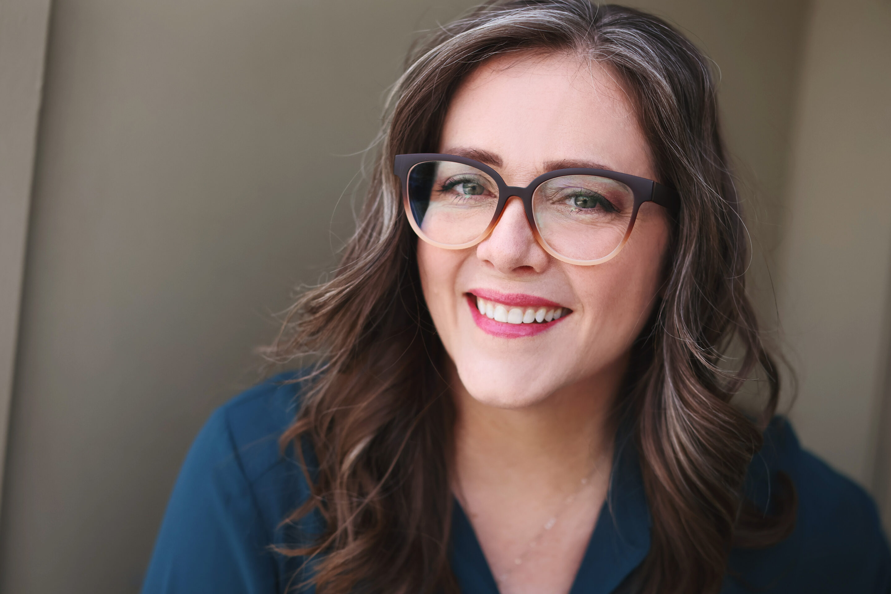 Angella Johnson wearing ombre colored glasses and a dark teal green shirt smiling against a beige background.